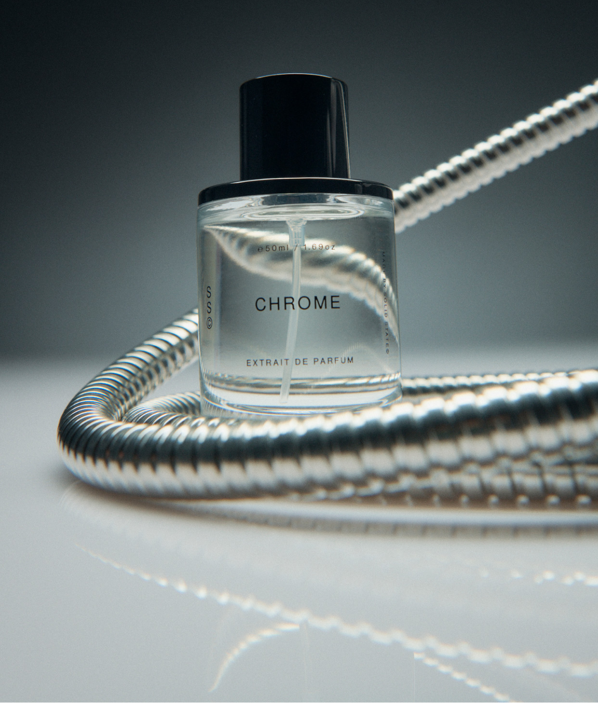 Perfume bottle labeled 'Chrome' with a metallic hose on a reflective surface.